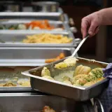 Eine Hand schöpft Kartoffeln aus einer Chafing Dish. Da fragt man sich, warum sagt man Mahlzeit? Leckeres Essen für alle!