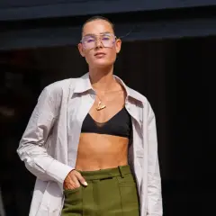 Frau trägt ein helles Hemd offen mit einem schwarzen T-Shirt darunter und einer grünen Hose.
