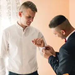 Ein Mann hilft einem anderen, die Manschettenknöpfe an seinem Hemd zu schließen, während er seinen Anzug trägt.