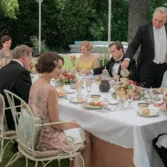 Gäste speisen im Freien, ein Butler serviert. Alle zeigen gute Manieren bei diesem eleganten Festessen.