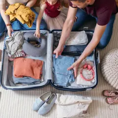 Familie packt gemeinsam eine Reisetasche. Kleidung, Nackenkissen und Reiseutensilien werden sorgfältig verstaut.