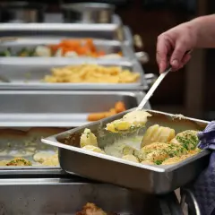 Eine Hand schöpft Kartoffeln aus einer Chafing Dish. Da fragt man sich, warum sagt man Mahlzeit? Leckeres Essen für alle!