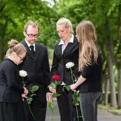 Trauernde Familie mit Rosen bei einer Beerdigung. Der Knigge zur Beerdigung wird hier durch stille Anteilnahme und respektvolles Gedenken gezeigt.