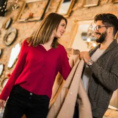 Ein Gentleman und eine Frau schauen sich lächelnd an, während sie Kleidung in einem Geschäft betrachten.