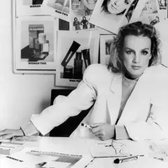 Jil Sander Designerin am Schreibtisch, umgeben von Entwürfen und Produktbildern ihrer Marke.
