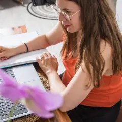 Frau mit Brille schreibt Notizen, während sie am Laptop arbeitet. Sie schafft sich eine gute digitale Ordnung für ihr Homeoffice.