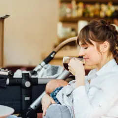Eine junge Mutter genießt eine Tasse Kaffee, während sie ihr Baby stillt. Der Kinderwagen steht daneben. Ein Moment der Ruhe beim Stillen im Restaurant.