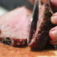 Ein Messer schneidet ein saftiges Steak auf einem Holzbrett. So schneidet man ein Steak richtig, um die zarten Fasern zu erhalten.