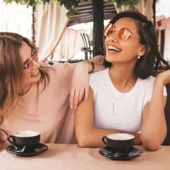 Zwei Freundinnen lachen bei Kaffee. Sie zeigen, wie gut man auf Komplimente reagiert: mit Freude und Selbstbewusstsein.