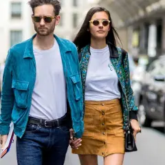 Ein Paar geht Hand in Hand, bereit für ein erstes Date. Er trägt eine blaue Jacke, sie einen gemusterten Blazer.