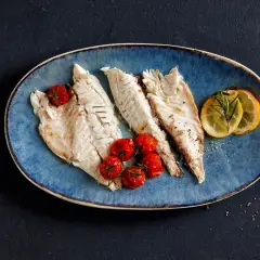 Drei zarte Fischfilets liegen auf einem blauen Teller, garniert mit Kirschtomaten und Zitronenscheiben. Perfekt zum Fisch filetieren am Tisch.