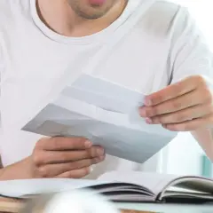 Mann öffnet Briefumschlag, was die Bedeutung von "c/o" in diesem Kontext verdeutlicht.