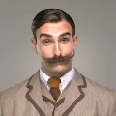 Ein Gentleman mit beeindruckendem Schnurrbart und kariertem Sakko blickt neugierig in die Kamera.