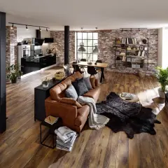 Gemütliche, offene industrial wohnung mit brauner Ledercouch, Holztisch, schwarzer Küche und Ziegelwänden.