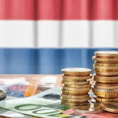 Münzen und Geldscheine liegen auf einem Tisch, im Hintergrund die niederländische Flagge. Ein Taschenrechner deutet auf die Berechnung von Trinkgeld in Holland.