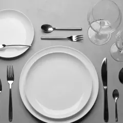 Einfach den Tisch decken: Zwei weiße Teller, Besteck und Weingläser liegen bereit für ein schönes Essen.