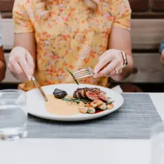 Gutes Benehmen bei Tisch: Eine Frau isst ein Steak mit Beilagen, während sie sich mit ihren Begleitern unterhält.