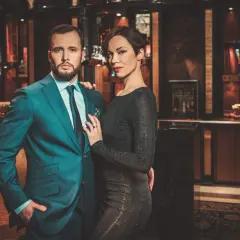 Ein eleganter englischer Gentleman im Anzug posiert mit einer Frau in einem glitzernden Kleid in einem luxuriösen Interieur.