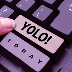 Ein Finger drückt die Taste "YOLO!". Was heißt YOLO? Das Leben ist kurz, also nutze den Tag!