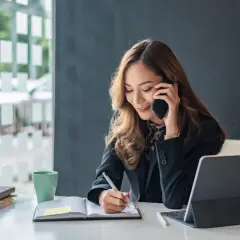 Eine Geschäftsfrau telefoniert und macht sich Notizen. Sie zeigt, wie man richtig telefonieren kann, während sie konzentriert arbeitet.