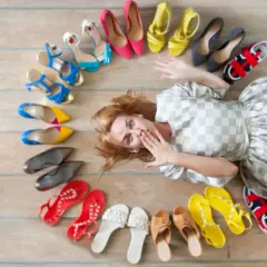 Frau liegt inmitten einer bunten Schuhsammlung, die sie gerade aussortiert. Von High Heels bis Sneakern ist alles dabei.