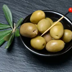 Grüne Oliven in einer Schale, bereit zum **Oliven essen**. Daneben ein Zweig mit Blättern.