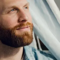 Mann mit Bart blickt nachdenklich nach oben. Hier sind einige tipps zur bartpflege für einen gepflegten Look.