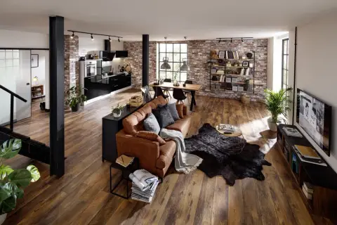 Gemütliche, offene industrial wohnung mit brauner Ledercouch, Holztisch, schwarzer Küche und Ziegelwänden.