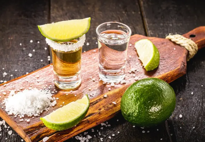 Zwei Tequila-Gläser, Salz und Limettenspalten auf einem Holzbrett. Die Tequila-Reihenfolge: zuerst Salz, dann Tequila, dann Limette.