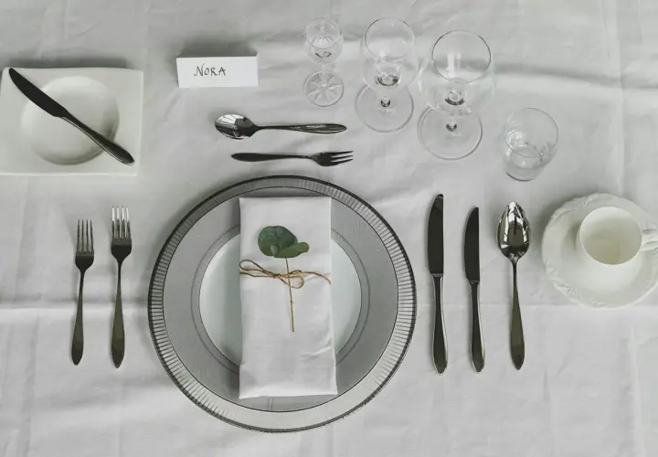 Elegante Tischdeko: besteck auflegen nur messer und gabel, mit Namenskarte "Nora" und einem grünen Blatt auf der Serviette.