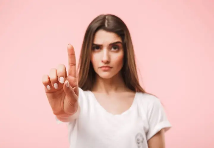 Frau hebt den Zeigefinger, als ob sie eine Einladung ablehnt. Ihre Miene ist ernst, die Antwort auf Absage Einladung ist klar.
