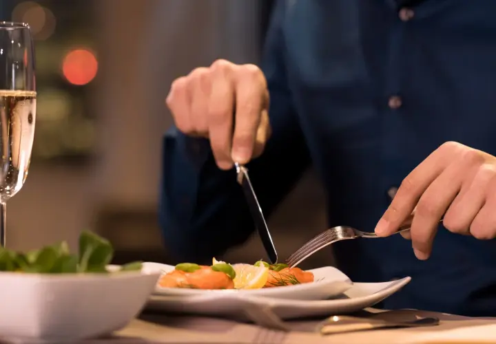 Mann isst Lachs mit Zitrone und Dill. Ein Glas Champagner steht daneben. So isst man stilvoll.