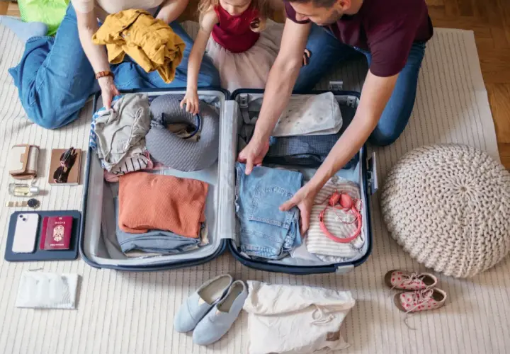 Familie packt gemeinsam eine Reisetasche. Kleidung, Nackenkissen und Reiseutensilien werden sorgfältig verstaut.