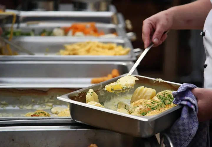 Eine Hand schöpft Kartoffeln aus einer Chafing Dish. Da fragt man sich, warum sagt man Mahlzeit? Leckeres Essen für alle!