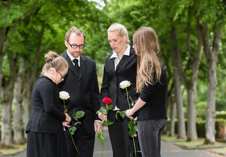 Trauernde Familie mit Rosen bei einer Beerdigung. Der Knigge zur Beerdigung wird hier durch stille Anteilnahme und respektvolles Gedenken gezeigt.