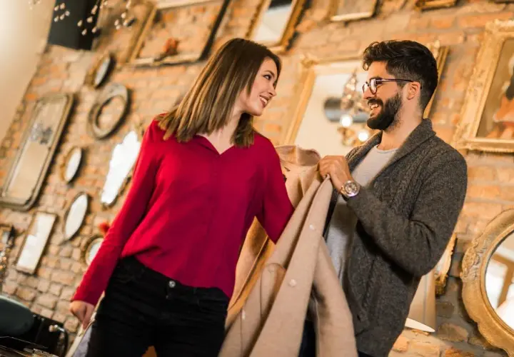 Ein Gentleman und eine Frau schauen sich lächelnd an, während sie Kleidung in einem Geschäft betrachten.