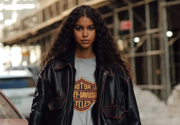 Junge Frau mit langen, lockigen Haaren trägt eine Lederjacke über einem Harley-Davidson-Shirt im Millennials-Style.