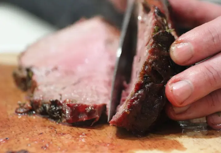 Ein Messer schneidet ein saftiges Steak auf einem Holzbrett. So schneidet man ein Steak richtig, um die zarten Fasern zu erhalten.