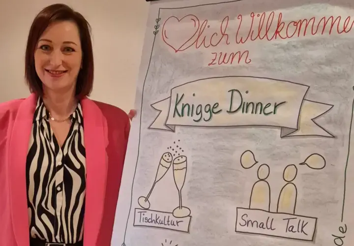 Frau in pinkem Blazer lächelt neben Flipchart mit "Knigge Dinner", Tischkultur und Small Talk.