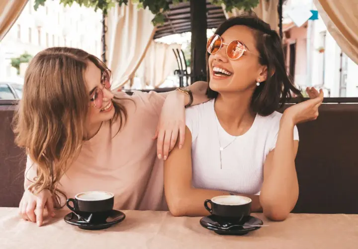Zwei Freundinnen lachen bei Kaffee. Sie zeigen, wie gut man auf Komplimente reagiert: mit Freude und Selbstbewusstsein.
