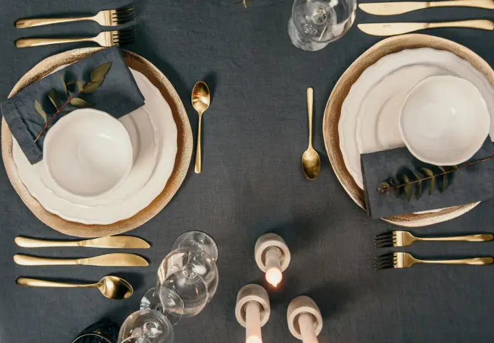 Elegante Tischdeko mit goldenem Besteck, das den Knigge-Regeln folgt. Teller, Gläser und Kerzen sorgen für festliche Stimmung.