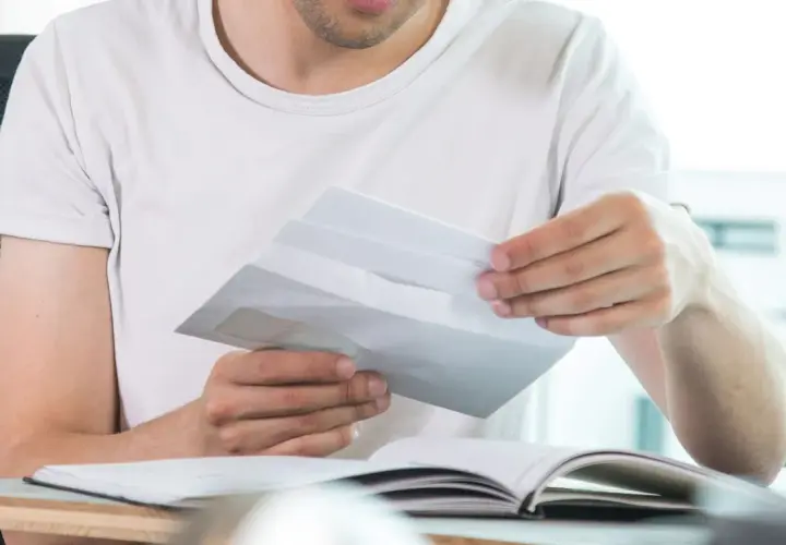 Mann öffnet Briefumschlag, was die Bedeutung von "c/o" in diesem Kontext verdeutlicht.