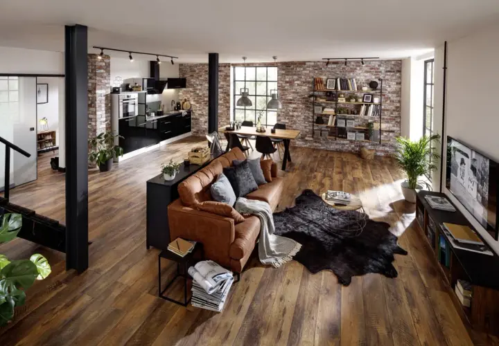 Gemütliche, offene industrial wohnung mit brauner Ledercouch, Holztisch, schwarzer Küche und Ziegelwänden.