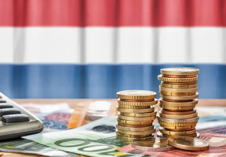 Münzen und Geldscheine liegen auf einem Tisch, im Hintergrund die niederländische Flagge. Ein Taschenrechner deutet auf die Berechnung von Trinkgeld in Holland.