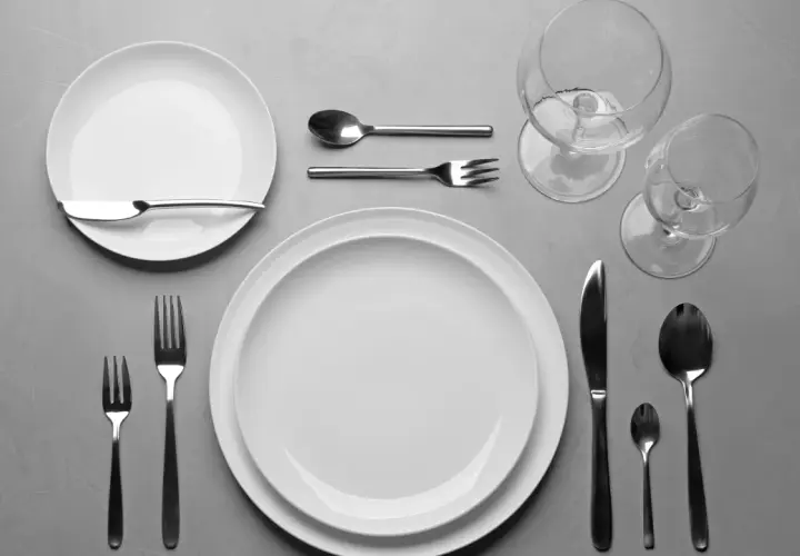 Einfach den Tisch decken: Zwei weiße Teller, Besteck und Weingläser liegen bereit für ein schönes Essen.