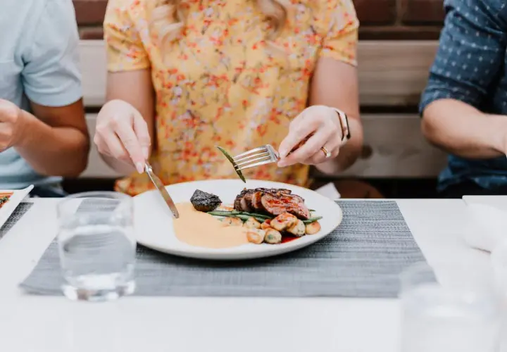 Gutes Benehmen bei Tisch: Eine Frau isst ein Steak mit Beilagen, während sie sich mit ihren Begleitern unterhält.