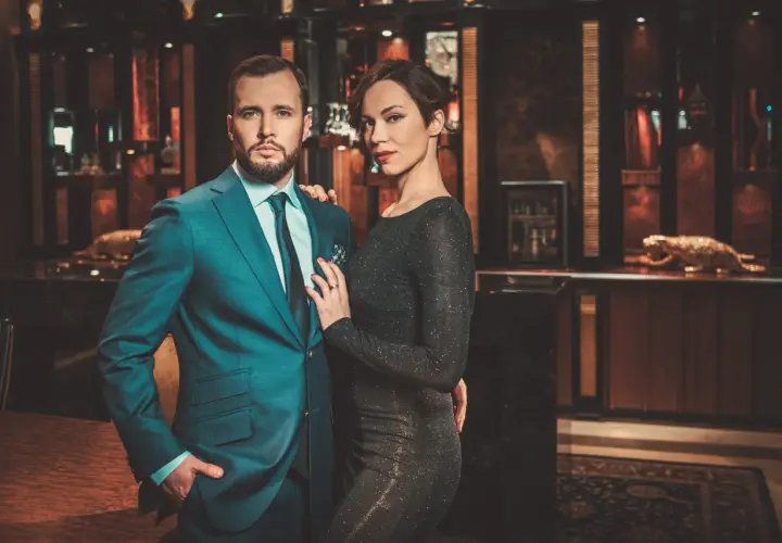 Ein eleganter englischer Gentleman im Anzug posiert mit einer Frau in einem glitzernden Kleid in einem luxuriösen Interieur.