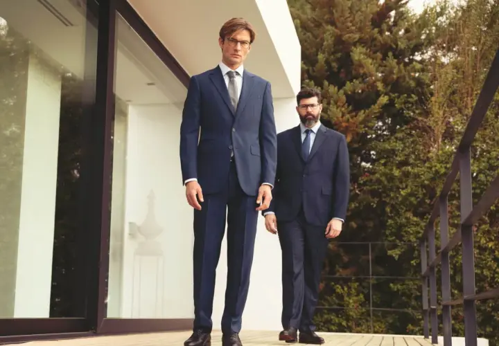 Zwei Männer in eleganten Anzügen stehen auf einer Holzterrasse. Sie zeigen, welche Schuhe zum Anzug passen: klassische Lederschuhe.