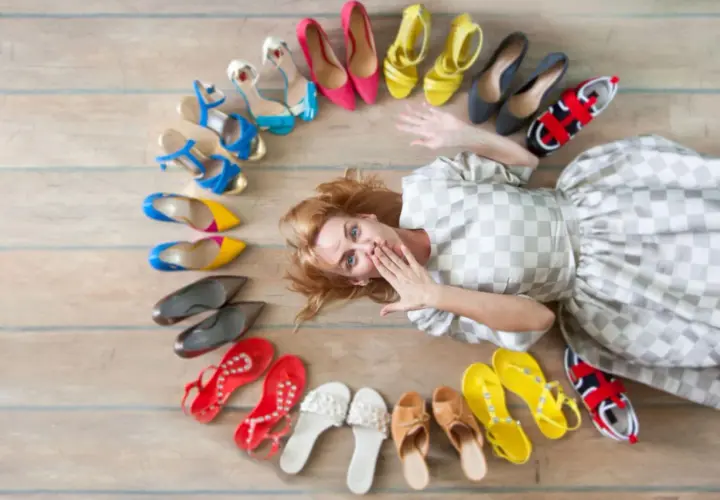 Frau liegt inmitten einer bunten Schuhsammlung, die sie gerade aussortiert. Von High Heels bis Sneakern ist alles dabei.