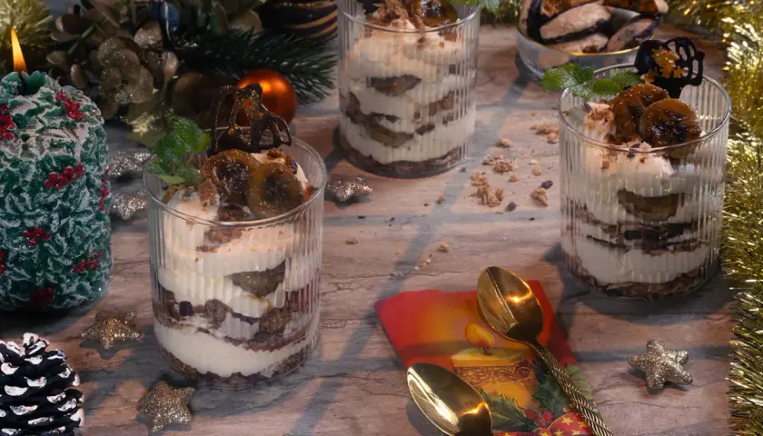 Festliche Gläser mit Schichten von Creme und Früchten, perfekt zum Dessert verzieren. Weihnachtliche Deko mit Kerze und Tannenzapfen.